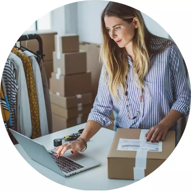 Woman typing on laptop while sealing box for shipping