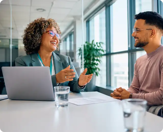 A female financial advisor with curly hair gesturing and smiling during a meeting with a male client.